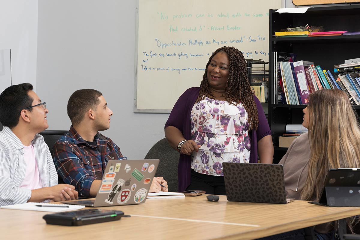 Gervlyne Auguste, assistant director of Binghamton University's McNair Scholars Program, works with students Eduardo Lezama, left, Hunter Akins and Elidenya Pena in the McNair lounge of the Tuscarora Office Building.