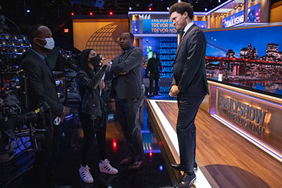 Jen Flanz works on The Daily Show set in New York City with Trevor Noah and correspondent Roy Wood Jr., center.