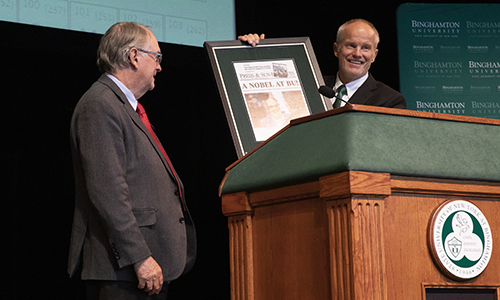 President Stenger holds up the framed front page of the Binghamton Press & Sun-Bulletin announcing Whittingham's Nobel Prize, another gift to the Nobel laureate.