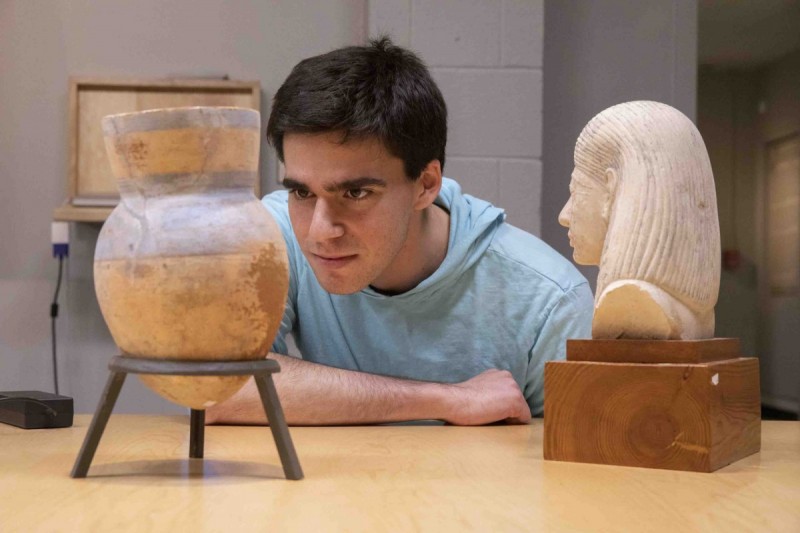 Binghamton University senior Doug Braun studies a vase and a bust from ancient Egypt for his curation project, 