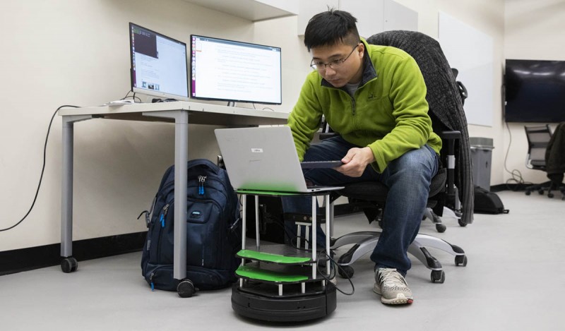 Researchers in Assistant Professor Shiqi Zhang's lab sent small robots through the Engineering Building to retrieve objects and then return as a human monitored their progress. With the robots is PhD student Yan Ding.