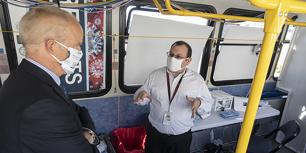 President Harvey Stenger listens as Michael Ponticiello, Broome County's director of emergency management, explains the process being used to test symptomatic county residents in a converted BC Transit bus that is currently stationed at the School of Pharmacy and Pharmaceutical Sciences at the University's Health Sciences Campus in Johnson City, N.Y.