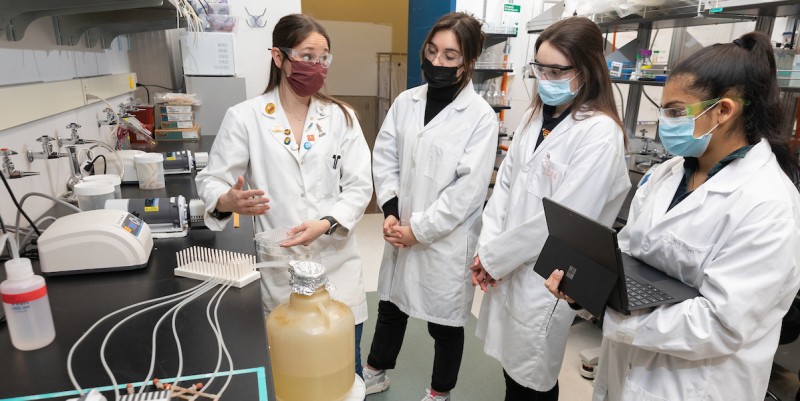 Research Assistant Professor Caitlin Light, at left, teaches Inessa Nicolo, Madison Muscente and Gayathri Nair, all independent study students and graduates of the First-year Research Immersion program, how to prepare a biofilm tube reactor that is used to grow biofilms.