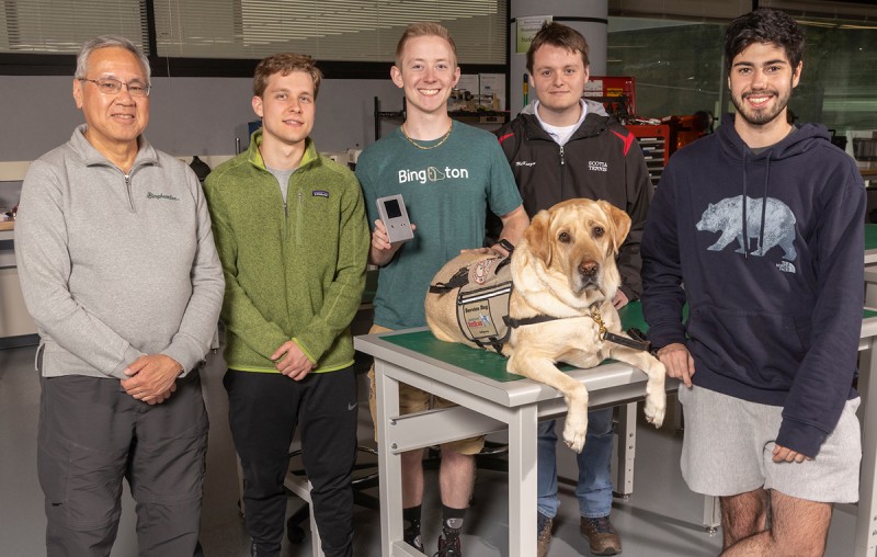 From left, Art Law, team advisor from Watson College's Department of Elec- trical and Computer Engineering; senior Benjamin Binisz- kiewicz; Eric Matson '22; and seniors Jacob McKenzie and Adam Cieszkowski meet Colonel Dave, a service dog owned by U.S. Army veteran John Coulton. All are involved in a project to build a medical alert device for Coulton.