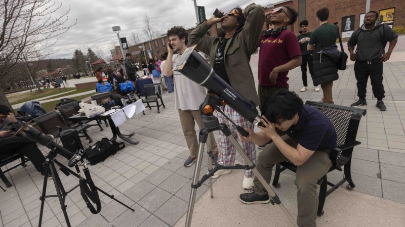 Midas Leung, front, looks at the solar eclipse through a telescope outfitted with a filter.