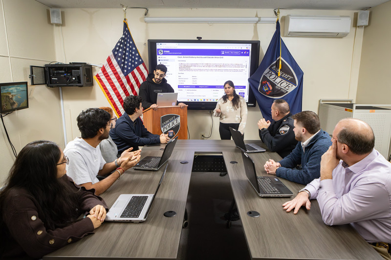 PhD student Mohammed-Khalil Ghali, MS ’24, and Shreya Agarwal, MS ’26, resent the Police Investigation Management System to, front to back at left, students Hemi Patel, Pranshu Desai, Sarah Escotto, and Abdelrahman Farrag; and front to back at right, Detectives Matt Brubaker and Jacob Harding and Chief Patrick Garey.