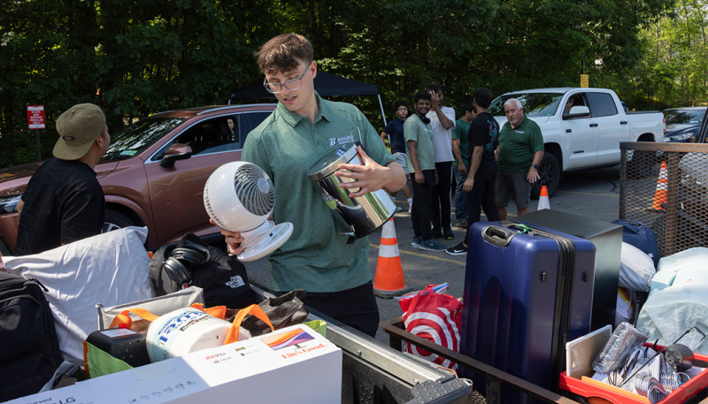 Declan Davis, a graduate student assistant for Residential Life, helps a family outside College-in-the-Woods at Binghamton University, Aug 14, 2026, during Move-in Weekend.
