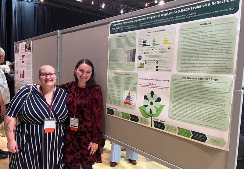 Renae Barber, community engagement outreach and assessment apecialist, and Kyra Hickey, community engagement coordinator, pose for a photo in front of their poster representing the LEAD Program at Binghamton University.
