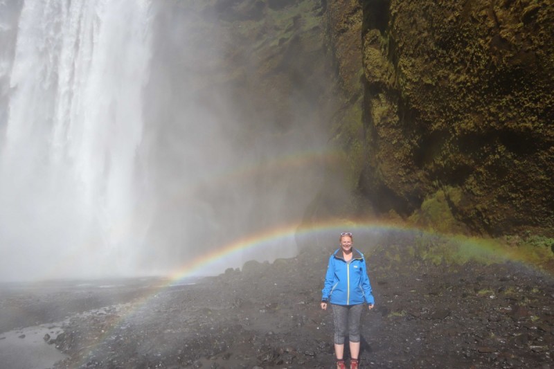Doctoral candidate Kennie Leet stands under a rainbow near a waterfall.