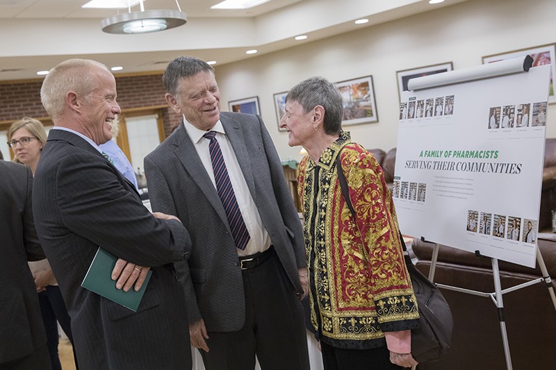 President Harvey Stenger speaks with Lisa Menner Brandt '66 and her husband, Dick, as they stand in front of a poster showing the many Menner family members who are pharmacists in Menner Brandt's native Austria.