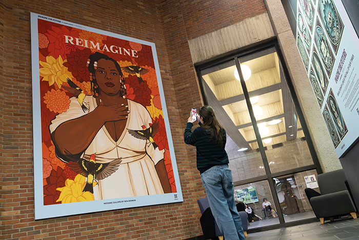 A student stands in front of a featured art piece in Bartle Library with a phone to utilize the Amplifier augmented reality app. The 