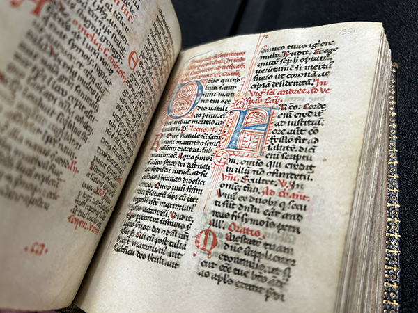 This book, recently acquired by Binghamton University, was written about 1350 by Franciscan friars in northern Italy, and later bound in Scotland around 1870. The 14th century breviary sits open-faced on a table displaying ornate script in Latin. The letters feature black ink as well as larger, artistic letters in red and blue ink.