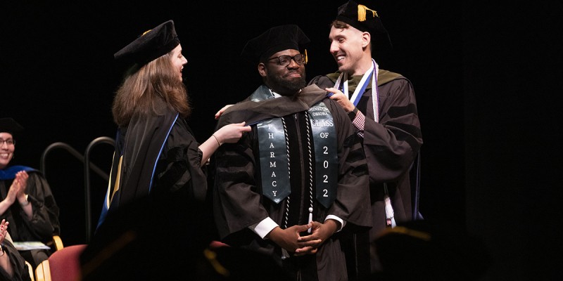 Clinical assistant professors Sarah Lynch and Bennett Doughty hood Doctor of Pharmacy graduate Chinedum Chiagozie Obiora at the School of Pharmacy and Pharmaceutical Sciences Commencement held Friday, May 13, 2022.