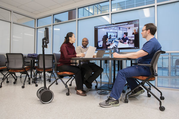 Decker graduate students (from left) Moon Ju Bae, Billy Manuel 
and Dan Fitzpatrick experience a healthcare team conference using video technology in the Southern Tier Telemedicine and Mobile Health Research Development and Training Center at Binghamton University. Their teacher, Assistant Professor Ann Fronzcek, participates via the remote telepresence robot.