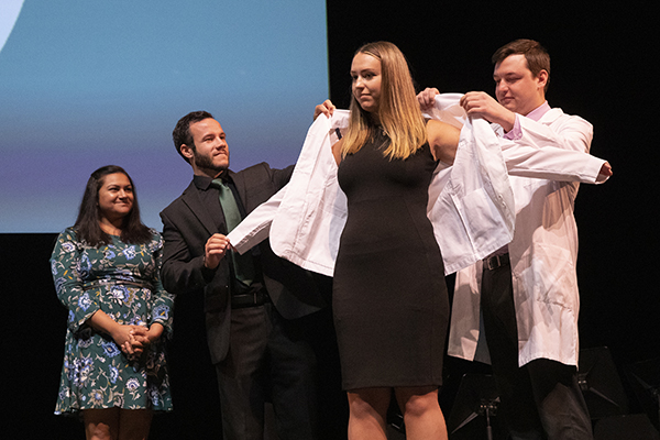 Hannah Surdi, is coated by her brother, Tyler Surdi, right, with assistance from Binghamton University Assistant Professor of Pharmacy Practice H Andrew Wilsey. Sara Spencer, clinical instructor and IPPE coordinator of pharmacy practice, looks on.