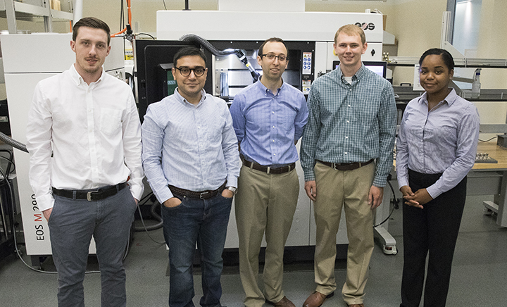 Assistant Professor Scott Schiffres (center) with students working in his lab in front of the 3D metal printer used for this research.
