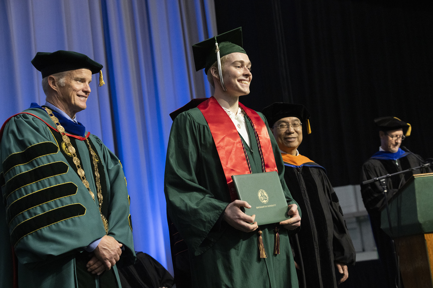 Flynn Anderson ’22 accepts his diploma from President Harvey Stenger, left, and Distinguished Professor Kaiming Ye, chair of the Biomedical Engineering Department, at May's Watson College Commencement ceremony.