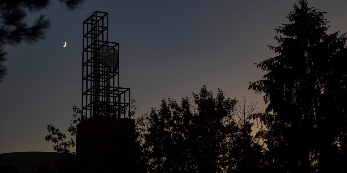 The Union Clock Tower at dusk with a crescent moon, framed by trees.