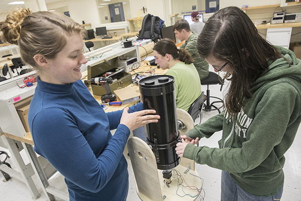 Emma Keeley, left, and Kietra Wiggins, right, work together to lift the telescope at the senior design center in the Glenn G. Bartle Library in late March. Drake Van Ornam and Oliver Hull are working in the background.