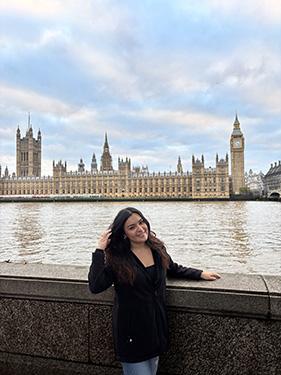 A women brushes her hair to one side while standing on a bridge with a river in the background