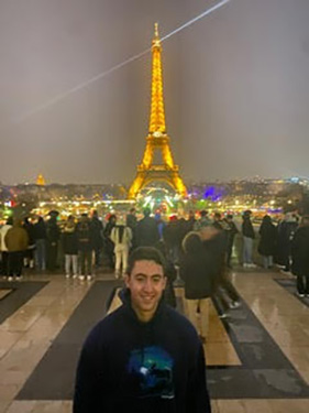 A man stands in front of the Eifel Tower illuminated at night