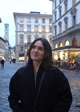 A woman looks up and to the left while wearing a dark coat on a city street