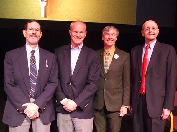 group of 4 men with blazers in front of dark background