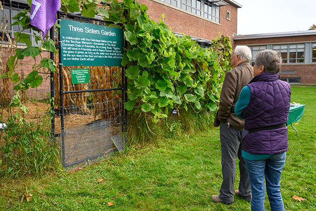 Two people observing a sign at a Three Sisters Garden with lush plants.