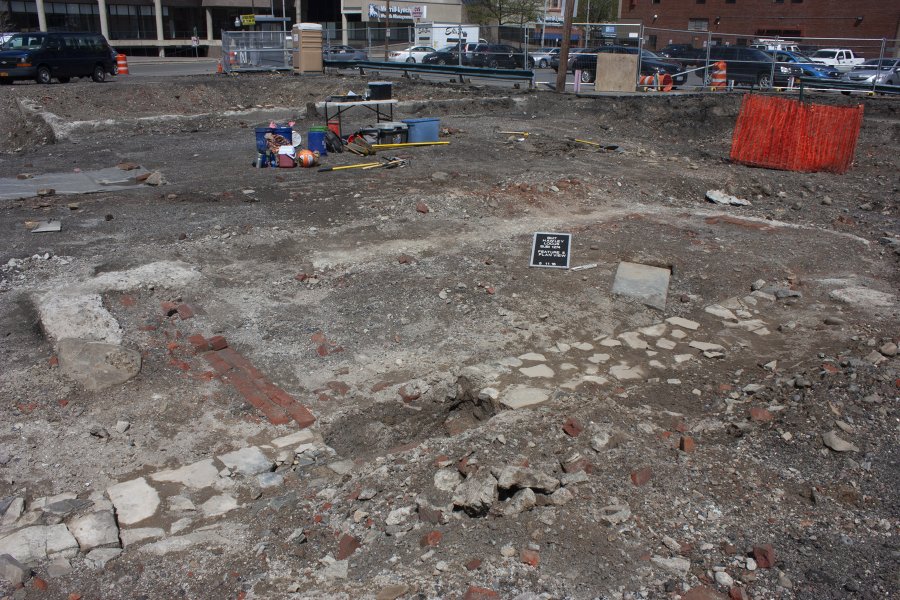 This foundation is a portion of the rear wall (with a concrete addition) of the line of commercial buildings along Washington Street built in the late 19th century. This section of foundation was part of 117 Washington Street, which for many years the late 19th century was James Prendergast’s tin and stove shop; it was later converted into a sausage factory. 