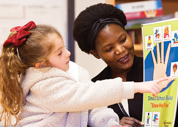 Faculty member reading with a child while using an educational communication board.
