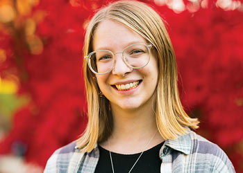Binghamton University student smiling outdoors on campus with colorful autumn foliage in the background.