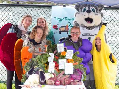 Students dressed as fruits and vegetables pose with baxter at a veggie tail gate event  photo