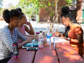 Three young black woman sit studying at an outdoor picnic table on campus photo