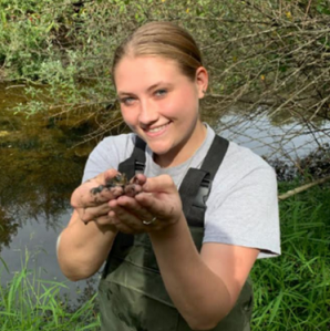 Brianna Sander smiles and holds up a brown frog for the camera